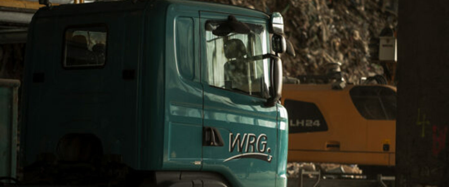 WRG-Lkw und Liebherr-Bagger in der Recyclinghalle vor einem großen Abfallberg.
