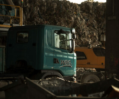 WRG-Lkw und Liebherr-Bagger in der Recyclinghalle vor einem großen Abfallberg.