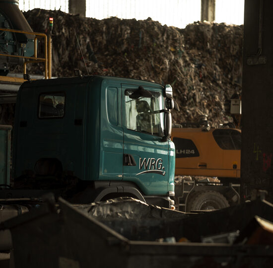WRG – Fahrzeuge in der Recyclinghalle WRG-Lkw und Liebherr-Bagger in der Recyclinghalle vor einem großen Abfallberg.