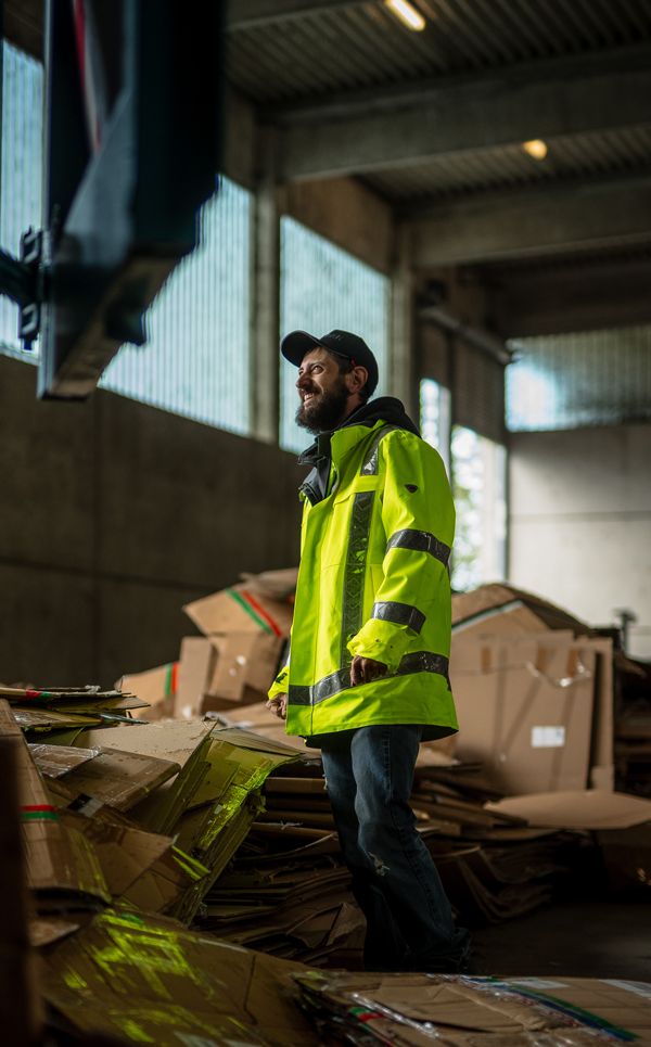 Mitarbeiter im Einsatz in der Halle Mitarbeiter steht in einer Recyclinghalle neben Kartonabfällen